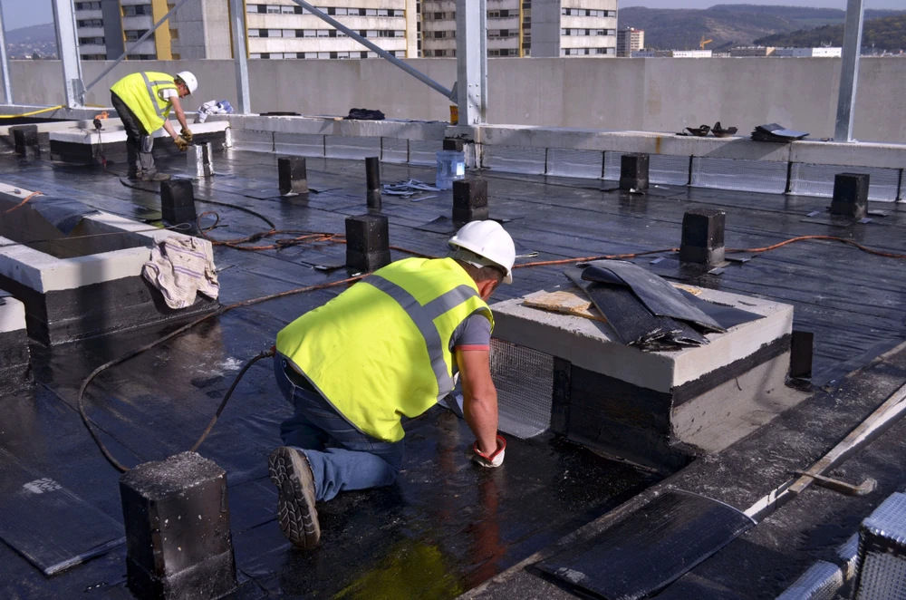 Ouvriers en équipements de sécurité haute visibilité effectuent des travaux d'étanchéité sur toiture-terrasse d'immeuble